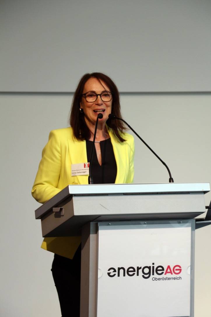 Frau spricht am Rednerpult der Energie AG, trägt Brille und gelben Blazer